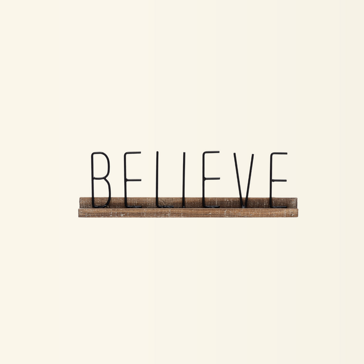 A decorative sign with the word "Believe" on a metal plate with a wooden base.