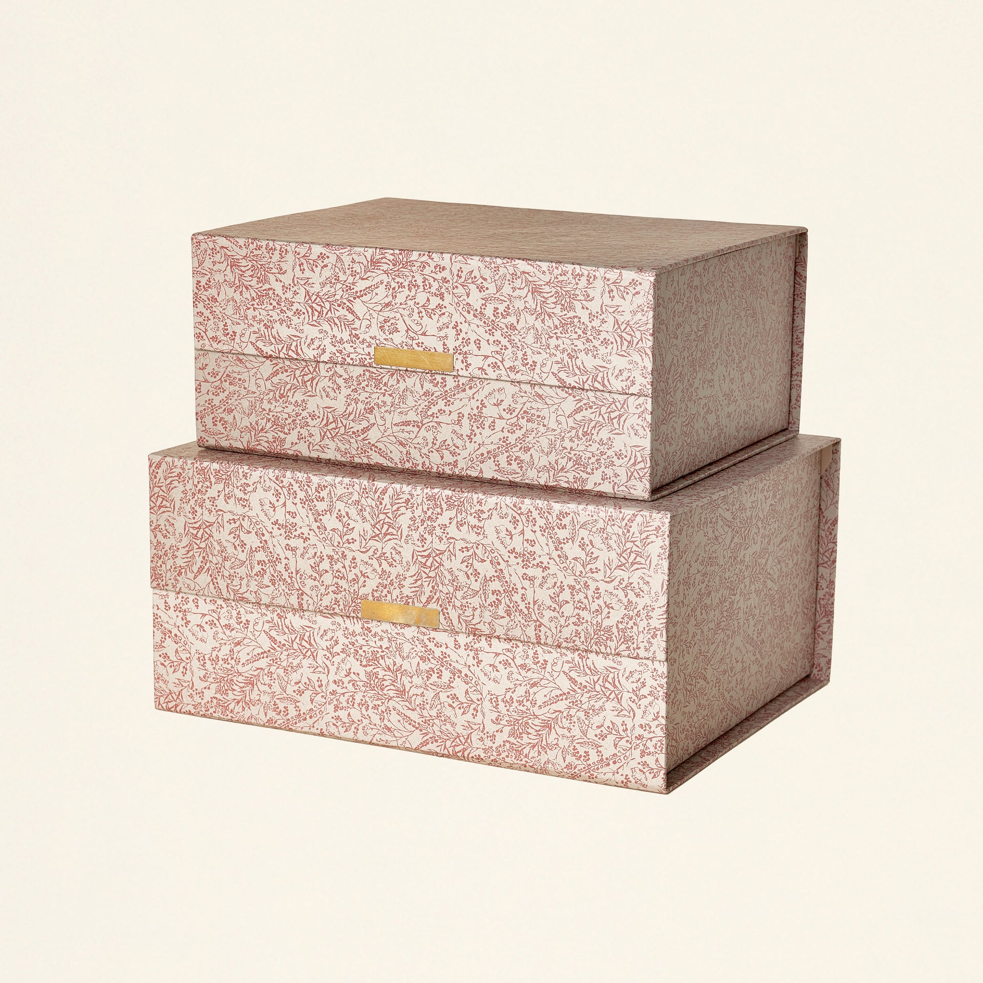 A set of two cardboard storage boxes with a grey and floral pattern and brass closures.