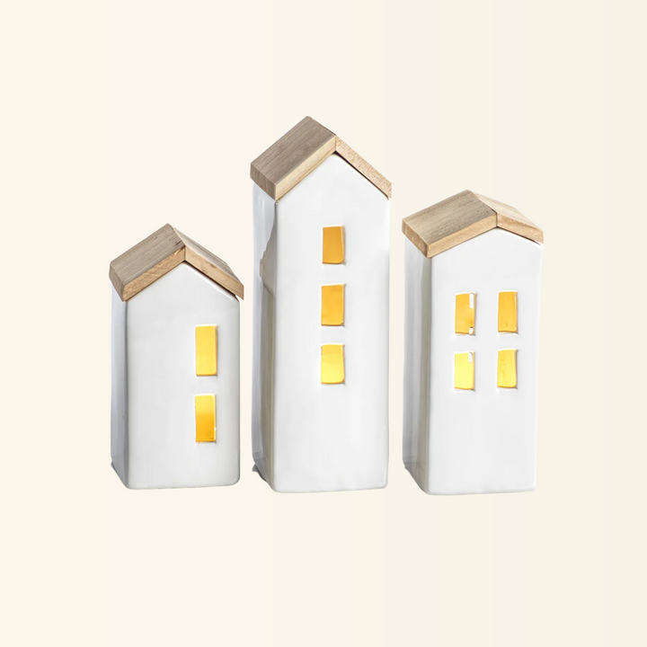 A set of three small ceramic houses with wooden roofs, illuminated by LED lights.